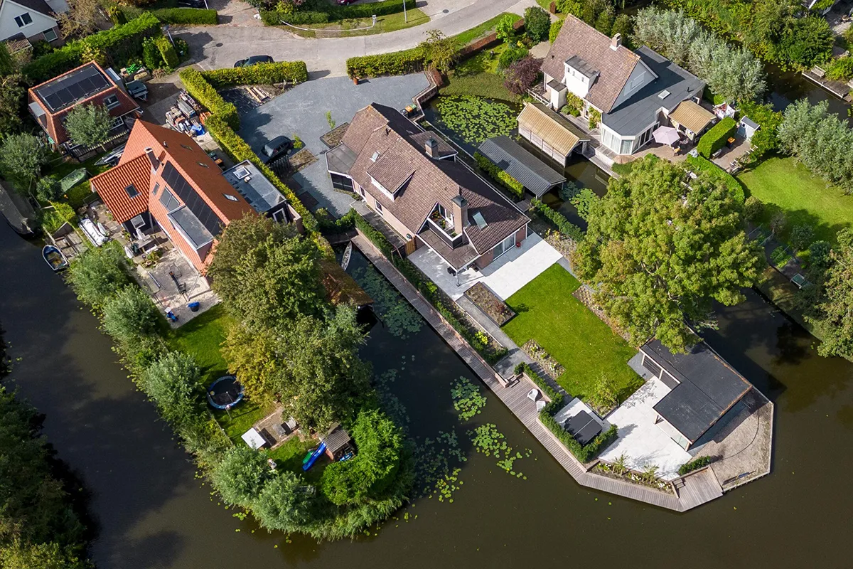 Oosterdelgebied met woningen langs water, groene tuinen en zonnepanelen op daken zichtbaar vanuit de lucht.